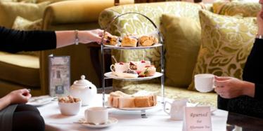 Afternoon Tea stand at Greenwoods Hotel with someone holding a cup of tea and someone else picking up a scone